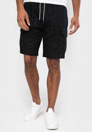 Schwarze Cargo-Shorts mit einem Kordelzugbund, ausgestattet mit Seitentaschen und einer lockeren Passform, kombiniert mit weißen Sneakers.