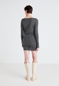 Gestreiftes Langarmkleid in Schwarz und Weiß, taillierter Schnitt, weicher Stoff, oberschenkellang, kombiniert mit knieb hohen beigen Stiefeln.