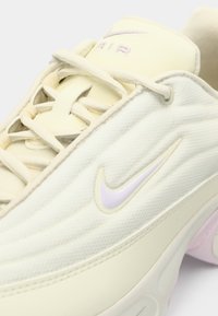Κοντινή λήψη παπουτσιού Nike Air σε κρέμα απόχρωση με υφασμάτινη υφή, κορδόνια και ανοιχτό μωβ λογότυπο Swoosh στο πλάι και στη γλώσσα.