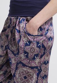 Lightweight, satin fabric pants with a dark blue base featuring a metallic floral and geometric pattern in purple and silver; includes side pocket.