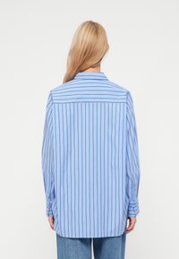 Kék csíkos ing sötétlila függőleges csíkokkal. Szabványos gallérral és hosszú ujjakkal rendelkezik, gombos mandzsettával, könnyű anyagból készült.