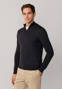 Donkergrijze sweater met een kwart-rits kraag, lange mouwen en een zachte textuur. Draag het met lichtbeige broek.