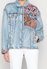 Světle modrá džínsová bunda s barevným vzorovaným nášivkem na pravé straně, dvěma předními kapsami a vyšívanými detaily na manžetách.