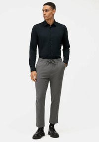 Camicia button-up blu scuro, pantaloni grigi con cordoncino, texture liscia, vestibilità slim. Scarpe nere stringate, design minimale, look casual.