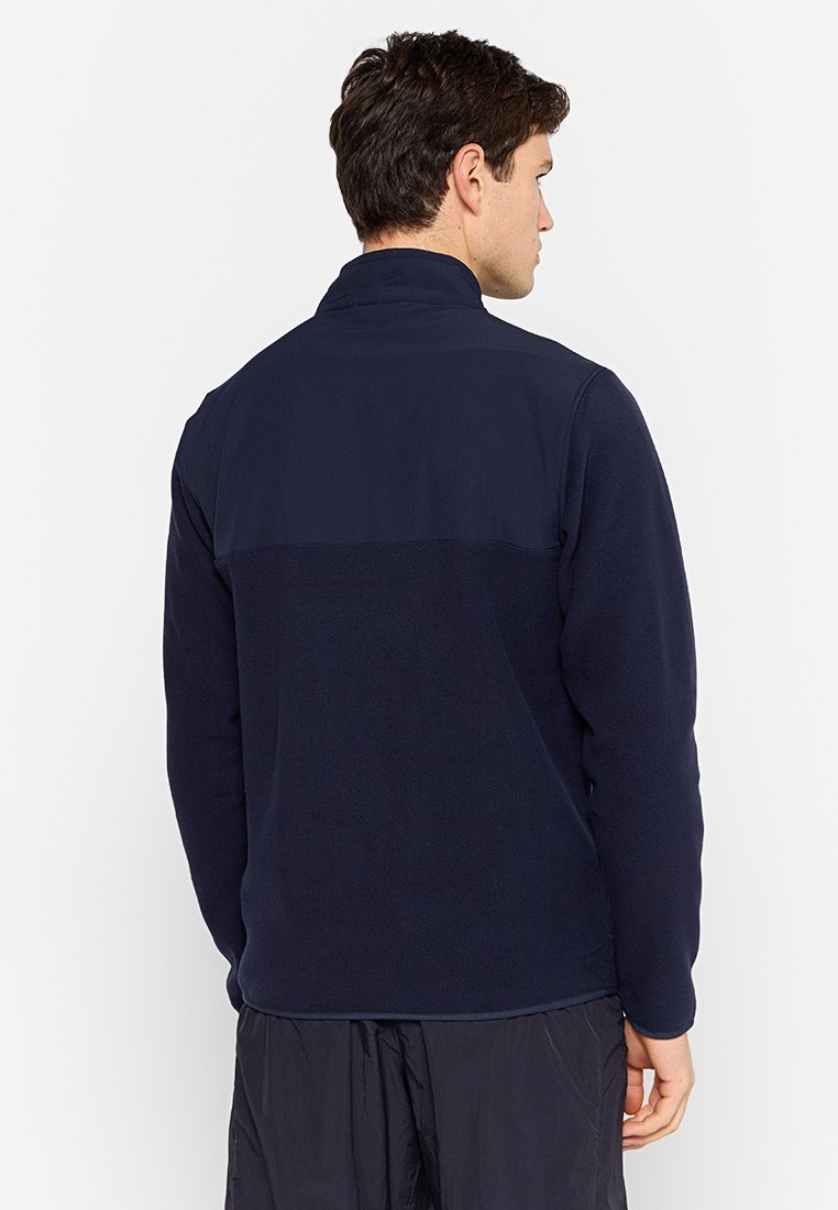 Marine fleece jack met een hoge kraag, textuurstof en contrasterend bovenstuk. Heeft lange mouwen en een rechte zoom.
