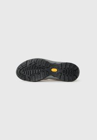 Czarna gumowa podeszwa buta z głębokim bieżnikiem i żółtym logo Vibram na środku, wyeksponowana na jednolitym białym tle.