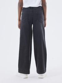 Jeans negros de pierna ancha con cintura alta, que cuentan con dos bolsillos traseros y un acabado limpio. Combinados con zapatillas blancas.