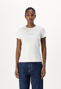 Balta medvilninė marškinė su trumpomis rankovėmis, kurių priekyje, krūtinės centre, yra mažas "Calvin Klein Jeans" logotipas. Paprasto apvalaus kaklo dizainas.