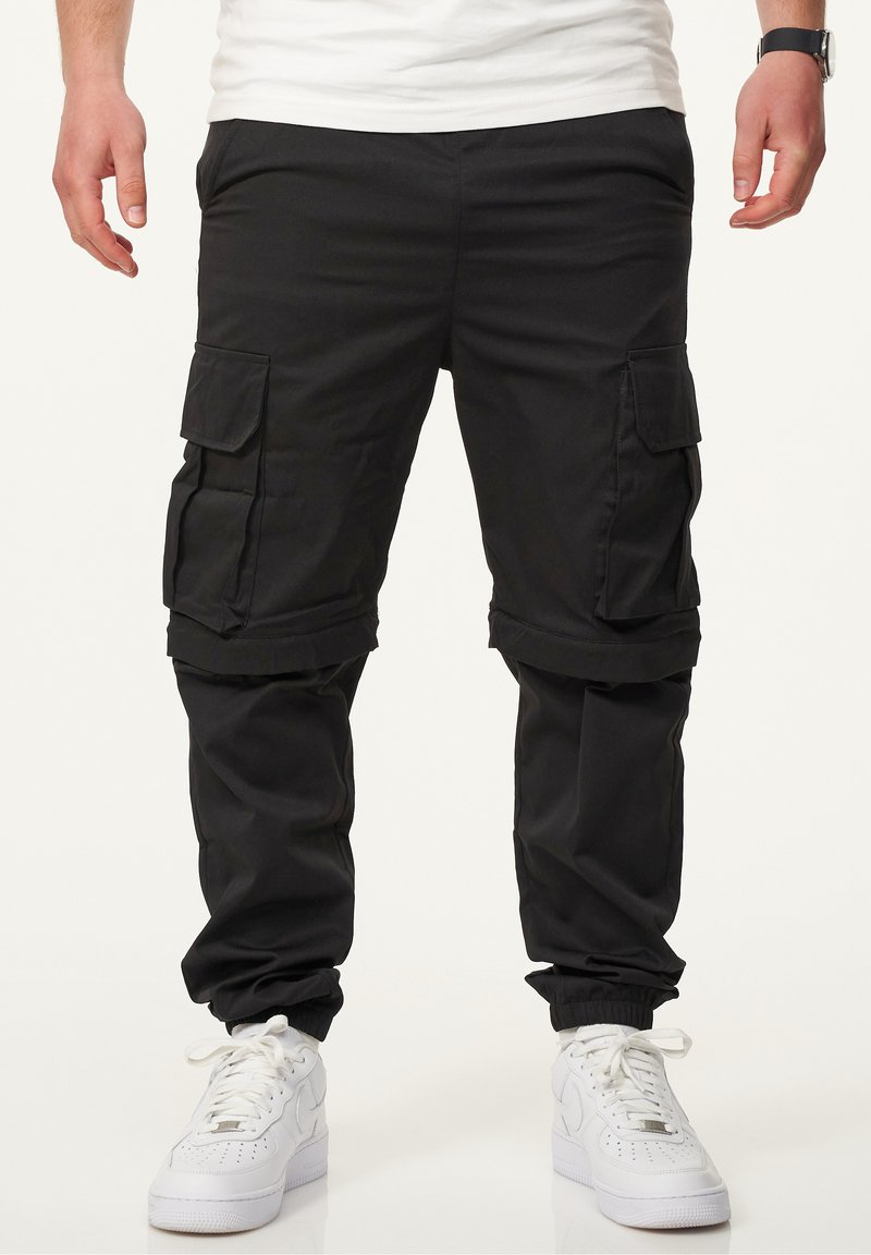 Schwarze Cargo-Hosen mit seitlichen Taschen, elastischen Bündchen und einem lockeren Schnitt, aus leichtem Stoff, kombiniert mit weißen Sneakers.