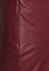 Bordeauxroter Lederrrock mit glatter Textur, dezentem Glanz und seitlichem Reißverschluss. Das Design zeichnet sich durch saubere Nähte und eine maßgeschneiderte Passform aus.