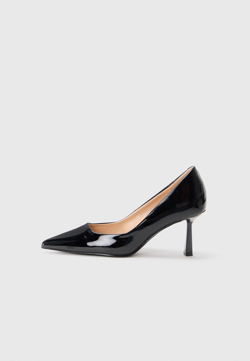 Melnas patent ādas augstpapēžu kurpes ar smailo purngalu un šauru vidējas augstuma stiletto papēdi uz baltas fona.