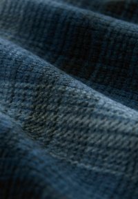 Țesătură texturată de culoare albastru închis, cu un model moale și canelat, formând falduri blânde și umbre.