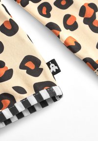 Leopardmönstrad tyg i beige, med orange och svarta mönster. Svart och vit randig nederkant med en liten svart etikett. Slett textur.