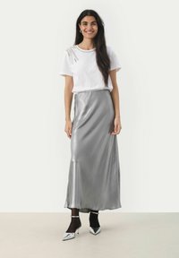 T-shirt bianco a maniche corte con decorazioni abbinato a una elegante gonna maxi in satin argento e décolleté argentati a punta.