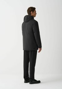 Schwarze Puffjacke mit Kapuze, ausgestattet mit einer glatten Oberfläche, elastischen Bündchen und einem lässigen Schnitt, kombiniert mit passenden schwarzen Hosen und Schuhen.