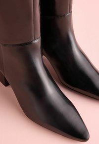 Czarne skórzane botki za kostkę z ostrym noskiem, słupkowym obcasem i błyszczącym wykończeniem. Gładka tekstura z minimalną ilością przeszyć.