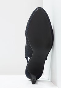 Zapato negro texturizado con punta afilada, que presenta un tacón delgado y lados elásticos, mostrando una suela lisa y plana. Talla marcada como 37.