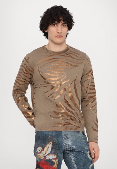 Bronze and beige sweater with a zebra stripe pattern, crew neckline, long sleeves, and a textured finish. Paired with graphic denim pants.