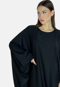 Schwarzes, übergroßes Kleid aus einem weichen, leichten Stoff mit weiten Ärmeln, rundem Halsausschnitt und seitlichen Taschen. Minimalistisches Design, glatte Textur.