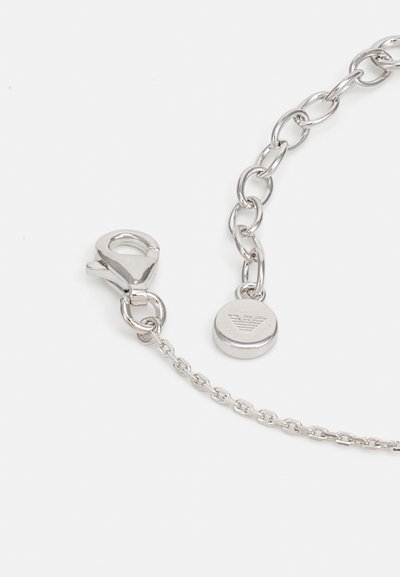 Silver metallkedja med en karbinlås. Inkluderar en rund tagg med ett präglat logotyp. Slät textur och enhetliga länkar.