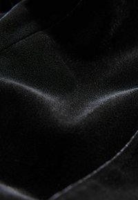 Tela de terciopelo negro con una textura suave y una superficie ondulante y lisa, que refleja la luz de manera sutil a través de sus pliegues ondulantes.