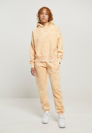 Hoodie i hlače s uzorkom prstenastog bojenja u breskvasnoj boji, s opuštenim krojem, teksturiranim materijalom i bijelim detaljima. U kompletu s kapuljačom na uzicu i elastičnim manžetama.
