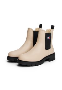 Bottines en cuir beige avec des côtés élastiques noirs, semelles épaisses en caoutchouc noir, doublure en shearling et logo Tommy Jeans sur le côté extérieur.