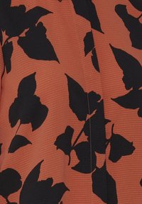 Tissu orange avec une surface texturée et des motifs de feuilles noires. Le design comprend plusieurs formes de feuilles et une couture centrale.