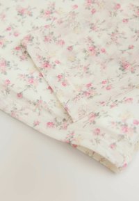 Tissu floral avec de petites fleurs roses et grises sur un fond crème clair. Texture douce et légère avec un détail de bord replié.