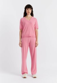 Maglione rosa lavorato a maglia con scollatura a V e maniche corte, abbinato a pantaloni a gamba larga coordinati. Entrambi i capi presentano una texture morbida.