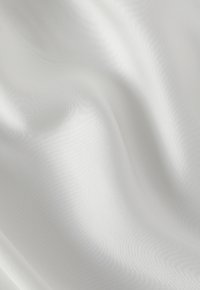 Bílá hedvábná tkanina, hladká a lesklá textura, s jemným leskem a drobnými vlnkami vytvářejícími jemné vlny po povrchu.
