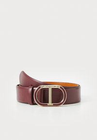 Maroon leather belt with a gold circular buckle featuring a 'T' detail, smooth texture, and a contrasting inner tan color.
