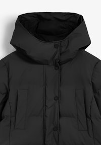 Zwarte gewatteerde jas met een hoge kraag, voorzien van knoopsluitingen en twee voorzakken. Gladde textuur, minimalistisch design.