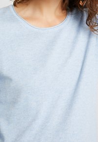 Pull bleu clair en tissu doux à texture côtelée, avec un col rond et une coupe décontractée, mettant en valeur les détails de couture réguliers.