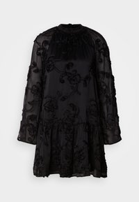 Crna haljina od prozirnog materijala, sa cvjetnim vezenjem i lepršavim rubom. Dugi rukavi s nabranim detaljima i visoki ovratnik.
