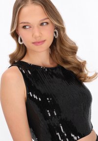 Fekete, flitteres rövid felső ujjatlan kialakítással és kerek nyakkivágással. Az anyaga fényes, amely visszatükröződő elemeket tartalmaz.