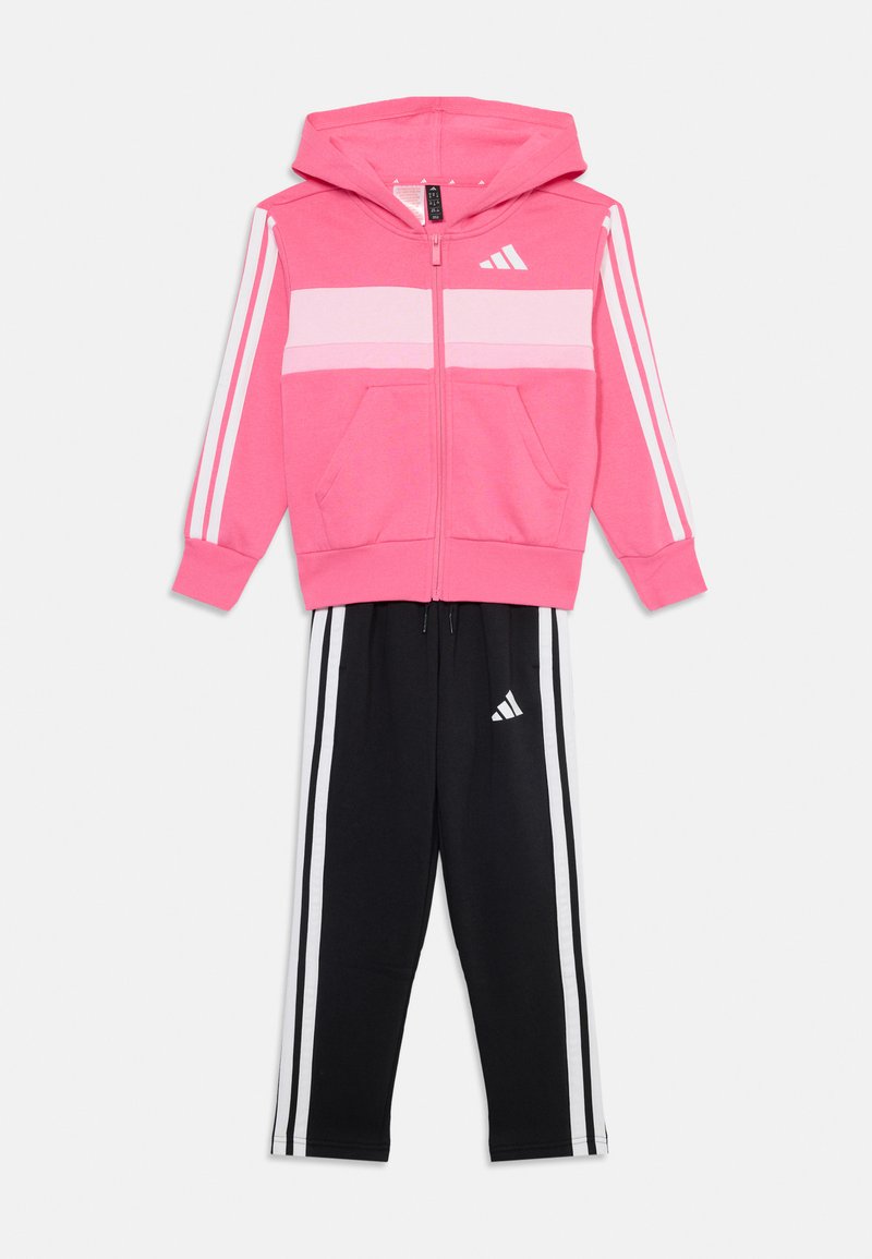 Pink zip-up hoodie with white stripes, front pockets, and black sweatpants with three white stripes and logo. Soft, athletic cotton blend.