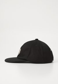 Casquette de baseball noire avec une visière plate et un petit design brodé sur le panneau avant, présentée de côté sur un fond uni.