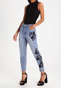 Hedvábný černý top bez rukávů v kombinaci s světle modrými džíny s černým květinovým vyšíváním po stranách. Černé sandály na vysokém podpatku.