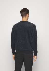 Tummansininen crewneck-huppari, joka on valmistettu pehmeästä, tekstuurista kankaasta. Siinä on ribbikuvioidut hihat ja helma. Minimalistinen muotoilu, ei huomattavia kuvioita tai yksityiskohtia.