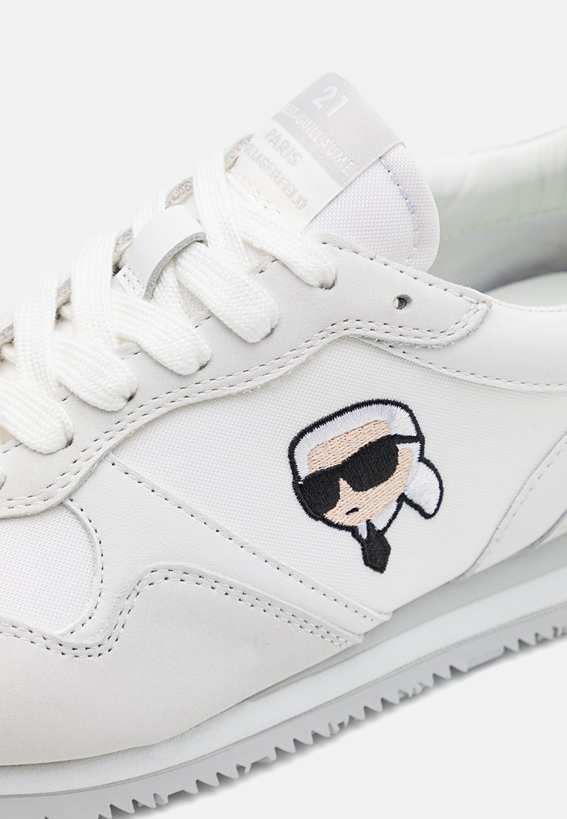 Zapatilla blanca con parte superior sintética, cordones planos, detalle de personaje bordado, suela de goma y lengüeta de textil etiquetada "21 PARIS".