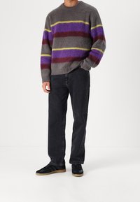 Maglione grigio a maglia con strisce viola, rosse e gialle, abbinato a jeans neri a gamba dritta e sneaker nere con suola color gomma.