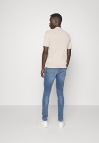 Polo de punto beige claro con mangas cortas, combinado con jeans ajustados azules y zapatillas blancas. Vista desde la parte de atrás.