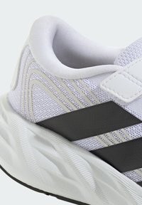Talons de chaussures de sport blancs et gris avec col matelassé, dessus en mesh, bandes noires et semelle blanche texturée.