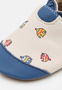 Zapato de cuero con una punta azul y parte superior en beige claro, que presenta patrones de peces coloridos en amarillo, azul, rojo y contornos negros.