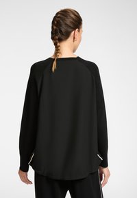 Zwarte langwerpige trui met een afgeronde zoom en contrasterende zijstrepen. Beschikt over een raglan ontwerp en een zachte textuur, getoond vanuit de achterkant.