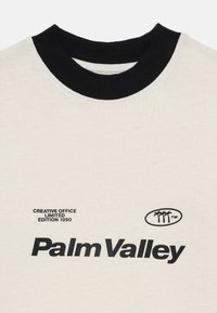 White cotton t-shirt with a black ribbed collar. Features "Palm Valley" logo and text "Creative Office Limited Edition 1990" in black print.