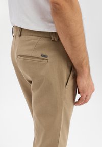Beige broek van gestructureerde stof, met een vlakke voorkant, rechte snit en een enkele achterzak met een klein metalen accent.
