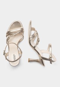 Sandali con tacco alto in metallo dorato, con cinturini incrociati, dettagli con fibbie e una finitura liscia. Il tacco è alto circa 7,5 centimetri.