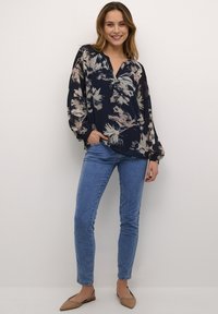 Blusa floreale navy con maniche lunghe, scollatura a V e dettagli con bottoni. Indossata con jeans skinny blu chiaro e ballerine beige.